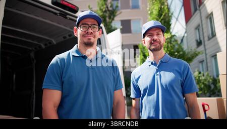 Uniformed Movers From Relocation Company Delivering Boxes To Happy Family. Stock Photo