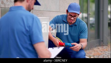 Experienced Hispanic Male HVAC Technician Installing Commercial Air Conditioning Unit. Stock Photo