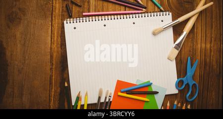 Flat design layout is showing blank notebook on wood table with pencils, paper, scissors, brushes Stock Photo