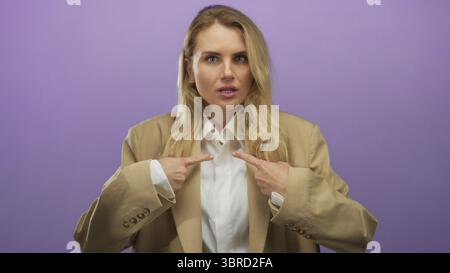 Woman in beige suit pointing at herself with a surprised expression against a purple isolated background, conveying bewilderment and curiosity in a mo Stock Photo