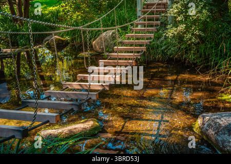 Small hanging bridge in a garden or park  over small river or pond Stock Photo