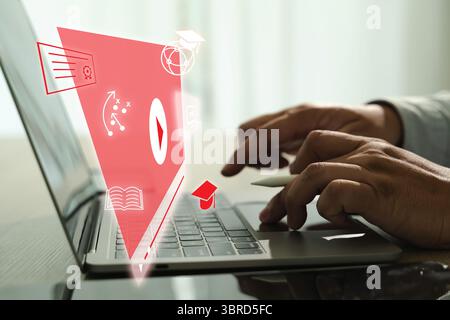 An educational video person using laptop with digital educational icons and graphics floating above keyboard, symbolizing online learning and digital Stock Photo