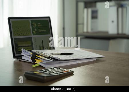 A report file eco friendly tidy office workspace with documents, pen, calculator, and laptop displaying charts and graphs, suggesting financial Stock Photo