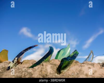 Pieces of glass used a protection in rural houses, cemented at the edge of the wall, with the sky as a background, in the town of Sora, in the eastern Stock Photo