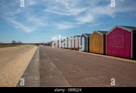 A long row of colourful beach huts stretches along the promenade bordering the sandy beach. Stock Photo