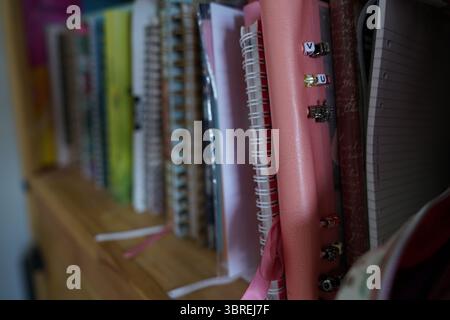 Colorful Spiral Notebooks Arranged on a Wooden Shelf with Accessories Displayed. Dorking, England Stock Photo