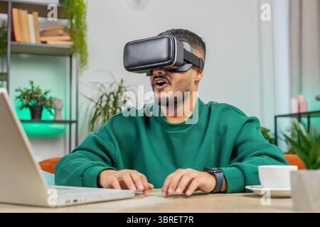 Indian man using virtual reality futuristic technology VR app headset helmet typing on virtual laptop keyboard, play simulation 3D 360 online video ga Stock Photo