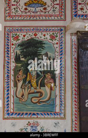Bikaner, India - 24 June 2025: View of an ornate wall mural depicting a deity with serene blues and vibrant yellows, framed by intricate floral patterns. Stock Photo