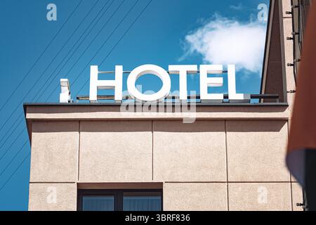 Hotel sign with white letters placed on a building roof with a window and with a blue sky in the background Stock Photo