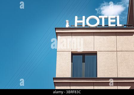 Hotel sign with white letters placed on a building roof with a window and with a blue sky in the background Stock Photo