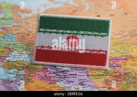Iranian flag made from fabric, placed on a world map highlighting Iran’s location. A concept of national pride, travel, and environmental awareness. Stock Photo
