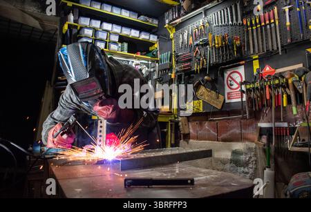 Worker with protective mask welding metal in workshop Stock Photo