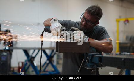 Metalworker using angle grinder, creating sparks while working on steel beam in industrial workshop Stock Photo