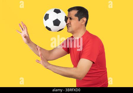 Man with red t-shirt playing sport being hit by a soccer ball with force in the face when he misses a catch or as an unexpected accident to a spectato Stock Photo