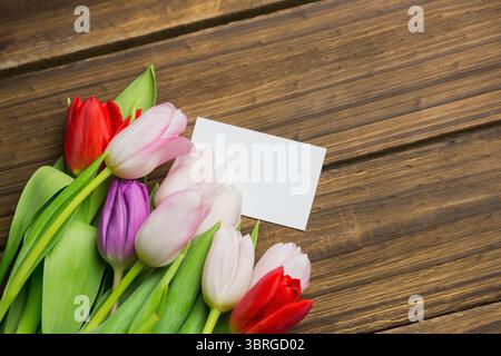 Multicolored tulip bouquet is being shown in flat design on plank tabletop with blank white card Stock Photo