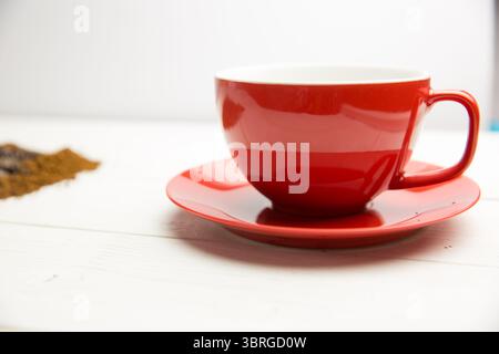 Flat design is showing red ceramic cup and saucer resting on wooden tabletop with scattered grounds Stock Photo