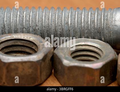 Close-up view of metallic nuts and bolts resting on a textured wood background. Stock Photo