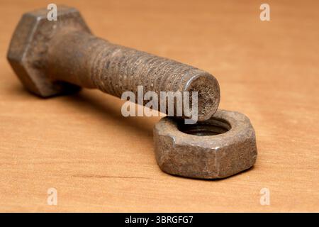 Close-up of a rusty bolt and nut resting on a wooden surface, showcasing wear. Stock Photo