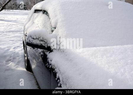 A parked car is completely covered in fresh white snow during winter. Stock Photo