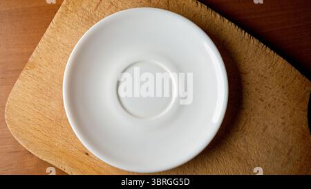 A simple white plate rests on a textured wooden surface, creating calmness. Stock Photo