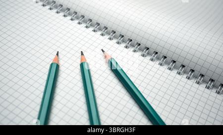 Three sharpened pencils lie beside an open notebook filled with squares. Stock Photo