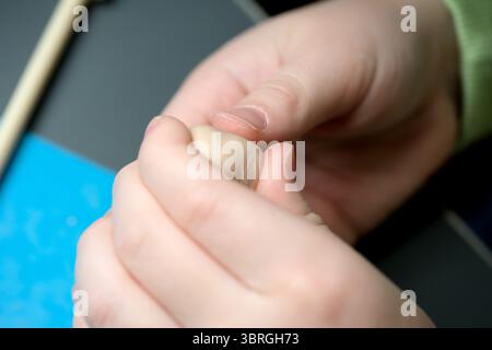Hands skillfully mold soft clay into a tiny figure during art time. Stock Photo