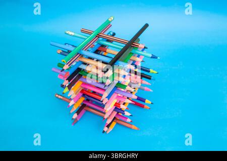 Stacked colored crayons stacked in the shape of a high tower illuminated  on blue Stock Photo