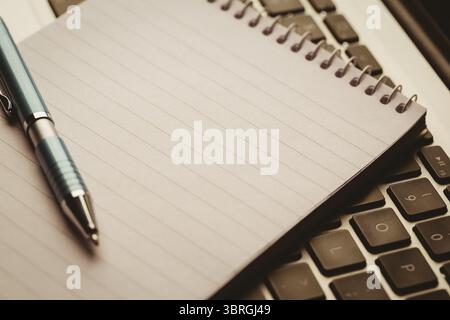 Spiral-bound notebook and ballpoint pen are resting on laptop keyboard in 3D render Stock Photo