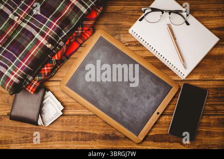 Small blank chalkboard is sitting in flat-lay arrangement, with shirts, wallet, notebook with pen Stock Photo