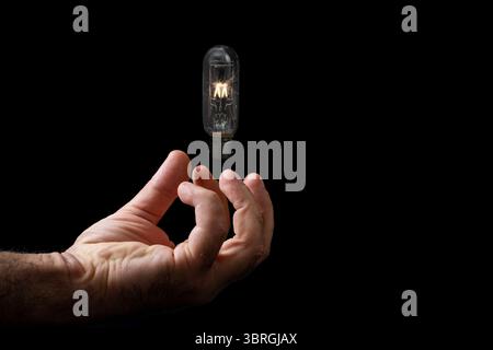 Male hand holding a lit levitating light bulb , isolated on black Stock Photo