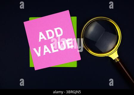 Add Value text on sticky note with magnifying glass on black background Stock Photo