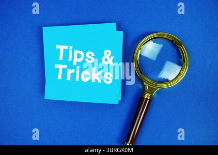 Tips and Tricks text on sticky note with magnifying glass on navy blue background Stock Photo