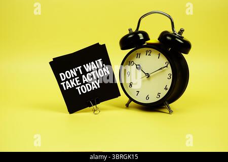 Don't Wait, Take Action Today text message on sticky note with alarm clock on yellow background Stock Photo