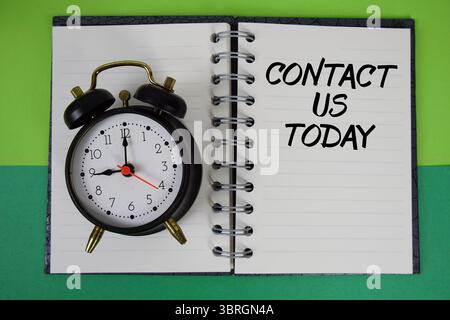 Contact Us Today text written on notebook paper with alarm clock Stock Photo