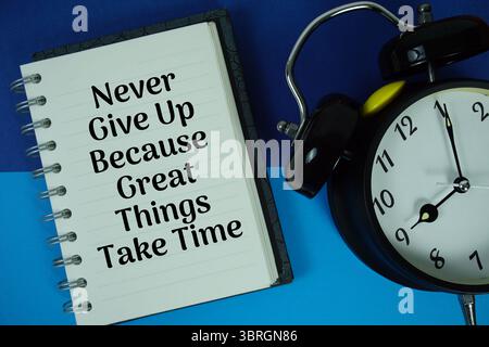 Never Give Up Because Great Things Take Time text written on notebook paper with alarm clock Stock Photo