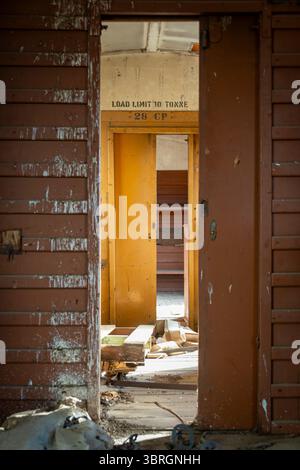 Looking down through two doors in an old, abandoned railway carriage, one door faded red, one yellow, with an old text sign "Load Limit 10 Tonnes" Stock Photo
