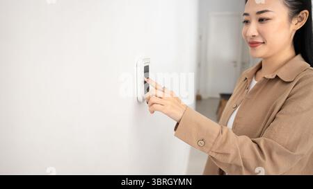 Woman pressing button on wall-mounted thermostat or smart control panel Stock Photo