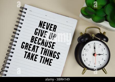 Never give up because great things take time text written on notepad with alarm clock Stock Photo