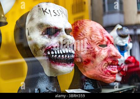 Scary Halloween masks for sale in a shop window, including a creepy white mask with Kiss Me written on the forehead. Grotesque horror masks. Stock Photo