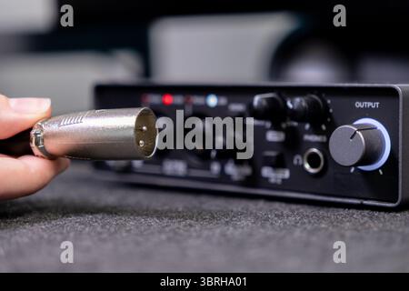 Close-up of a hand plugging a male XLR connector into a dark audio interface with visible OUTPUT knob, perfect for home studio recording or live sound Stock Photo