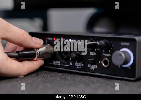 Detail view of a person connecting an XLR cable to a black audio interface, showing D-PRE microphoneline input, gain, and headphone output for sound e Stock Photo