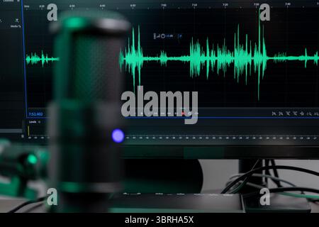Vibrant green audio waveform on monitor and professional desktop microphone, showcasing a studio setup for sound recording and content creation Stock Photo