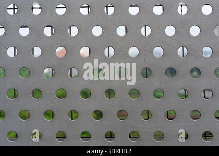Gray metal plate with a grid of perfectly aligned circular holes. Perforated steel sheet creating an abstract, industrial, Stock Photo
