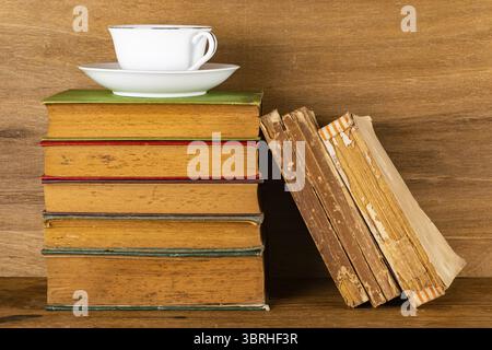 Closeup view stack of colorful old books and shabby damage old books with white ceramic coffee cup on wooden table Stock Photo