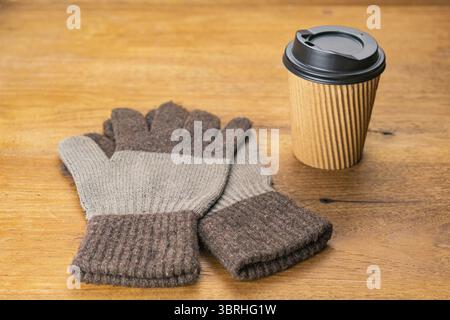 High angle view a pair of cloth gloves and a black plastic cap paper takeaway cup of hot coffee on wooden table in winter season Stock Photo