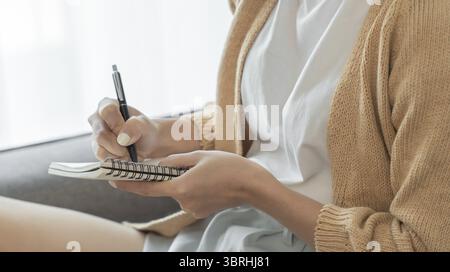 Asian Business woman working from office taking reading and writing notes in note pad Stock Photo