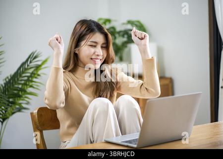 Happy young Asian Woman Successful working with laptop checking happy congrats get good news Young asian feel excited and colleague student passed exa Stock Photo