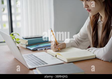 Asian woman using laptop to study student engaged in online learning at college Stock Photo