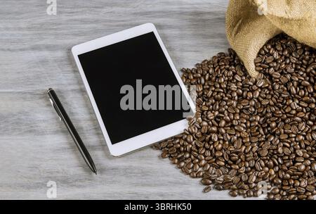The tablethone and pen lies next to coffee beans on table Stock Photo