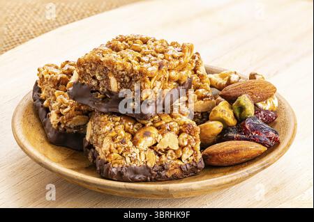 High angle view of crispy homemade peanuts, almond and chocolate mini protein bars and pile of mixed fruit and nuts in wooden dish on wooden board Stock Photo